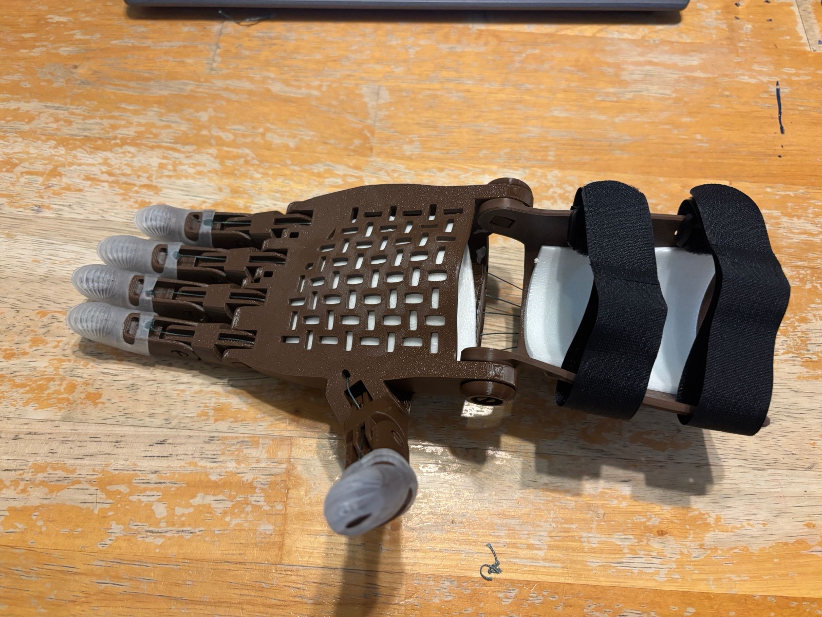 A finished 3D-printed hand in brown with clear gecko-grip fingertips and black straps