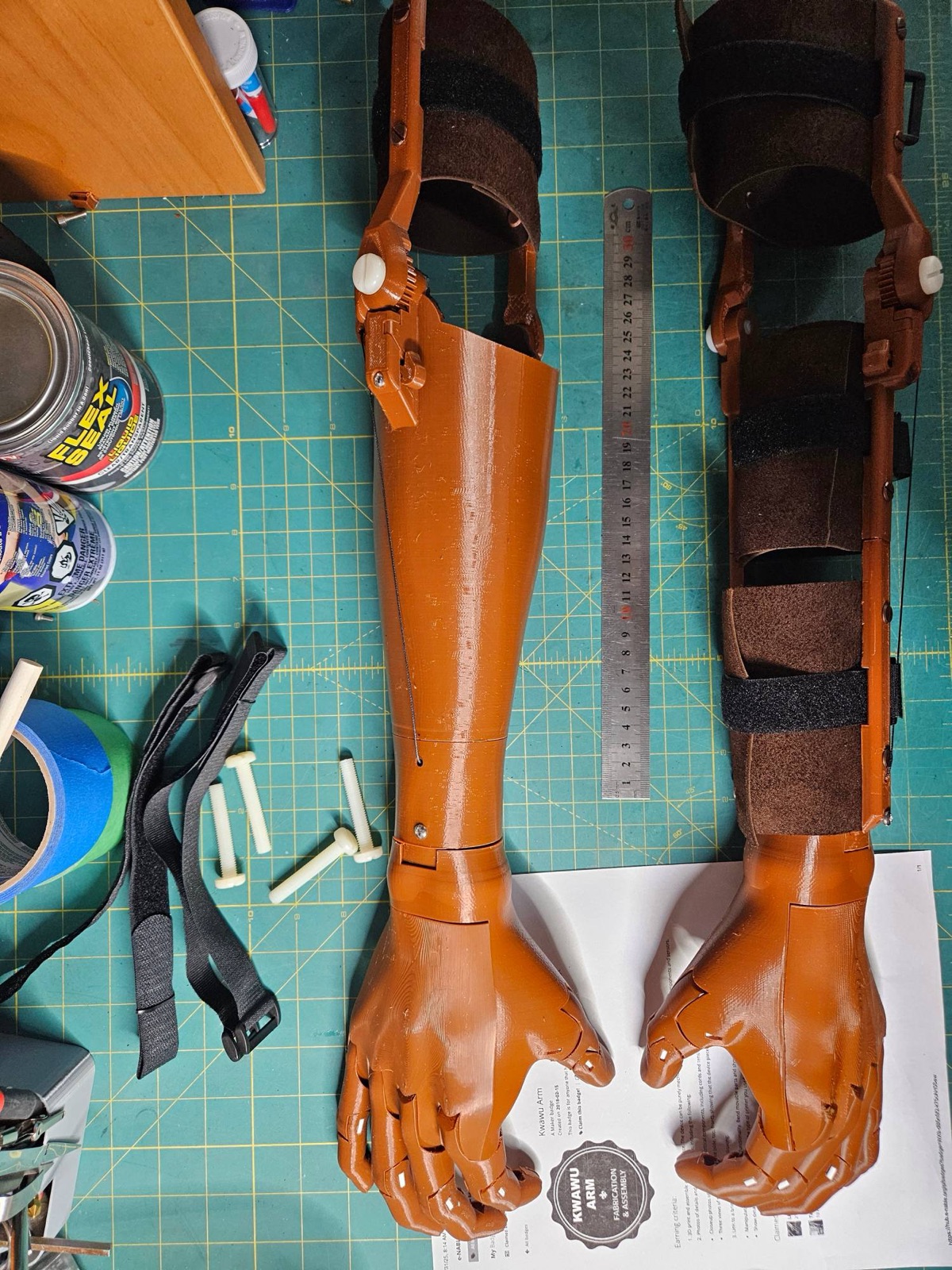 Two finished Kwawu arms in copper laid out next to a ruler